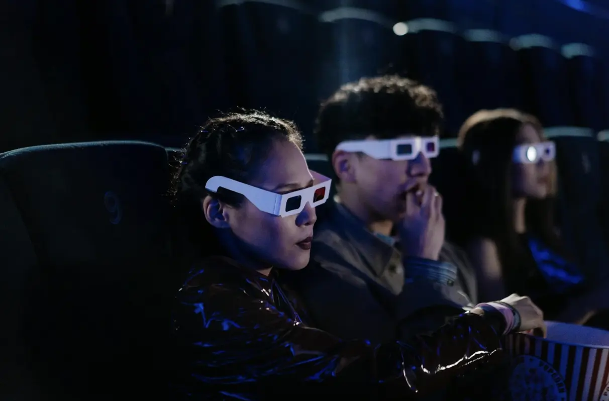 Friends enjoying a 3D movie night at the cinema, wearing glasses and eating popcorn.